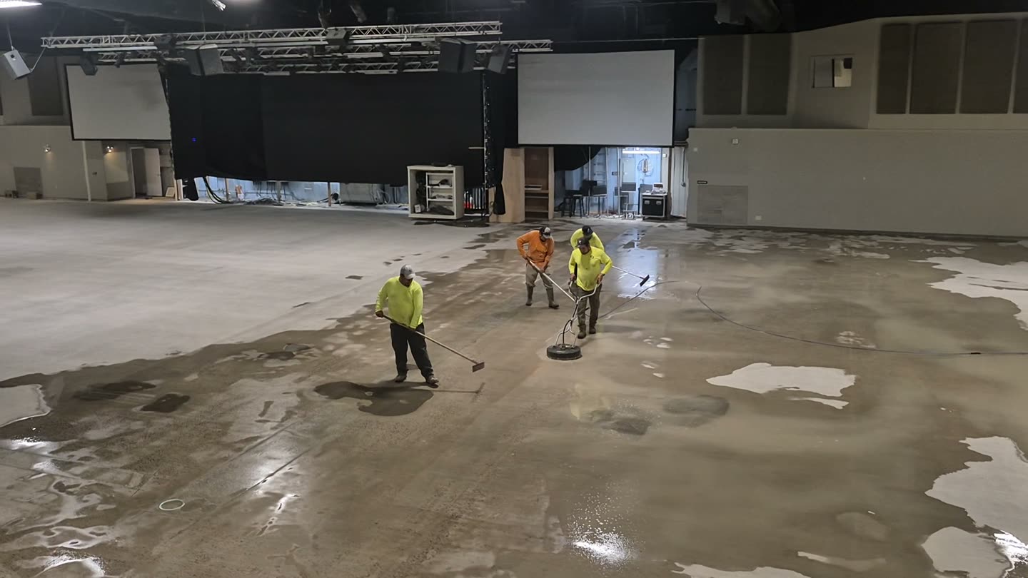 Three workers clean the exposed floor inside Agora KC during preparation of the space.
