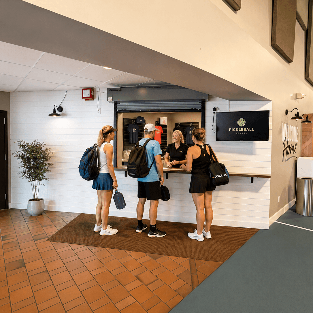 People with sports bags entering a building with a reception desk.